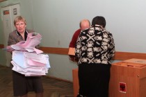 Представительница избирательной комиссии вынимает бюллетени из комплекса обработки избирательных бюллетеней (КОИБ)